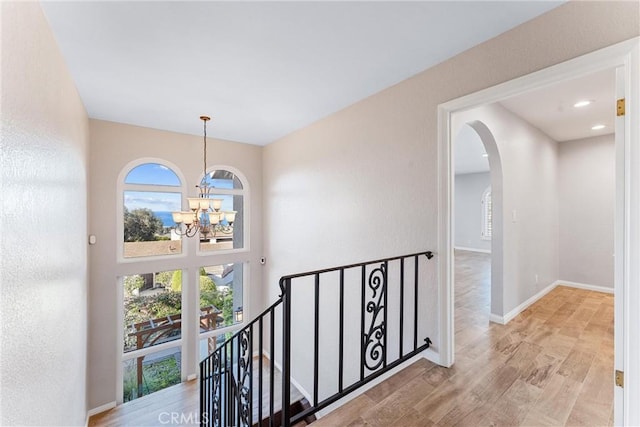 corridor with arched walkways, plenty of natural light, a notable chandelier, and an upstairs landing