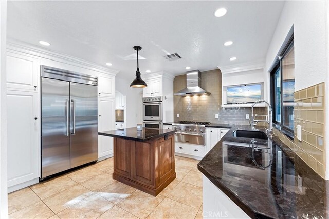 kitchen featuring wall chimney range hood, white cabinets, a sink, stainless steel appliances, and backsplash