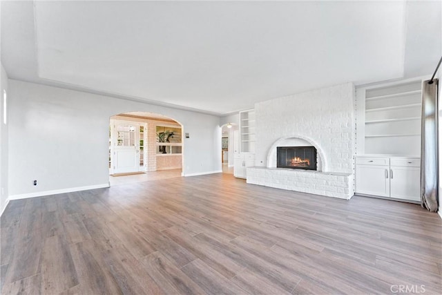unfurnished living room with baseboards, arched walkways, built in features, and wood finished floors