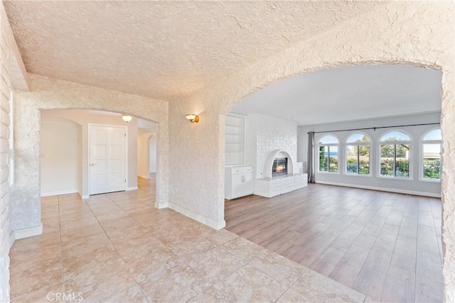 unfurnished living room with arched walkways, a fireplace, and a textured ceiling