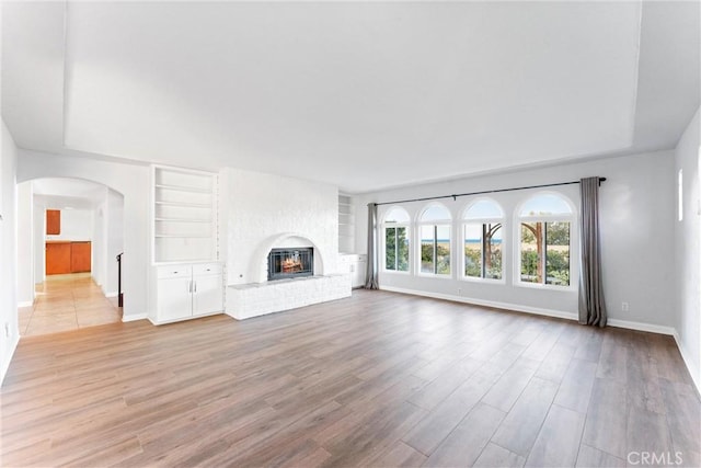 unfurnished living room with baseboards, arched walkways, a fireplace, and light wood-type flooring