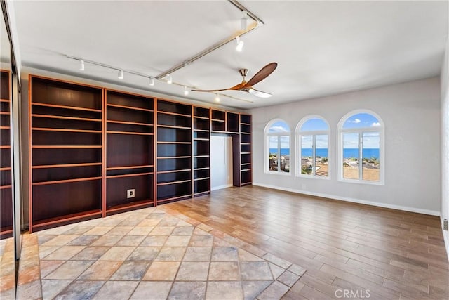 empty room featuring a ceiling fan, baseboards, track lighting, and wood finished floors