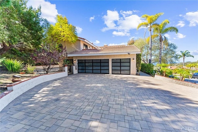 view of front of property featuring stucco siding, an attached garage, a tile roof, and decorative driveway