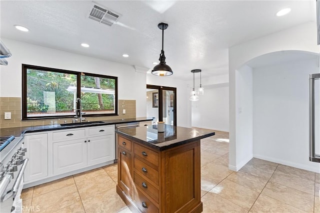 kitchen featuring visible vents, decorative backsplash, arched walkways, a sink, and high end range