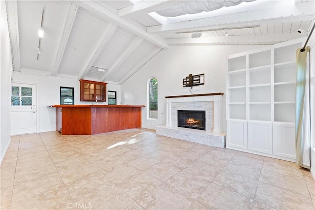 unfurnished living room with a glass covered fireplace, high vaulted ceiling, and beamed ceiling