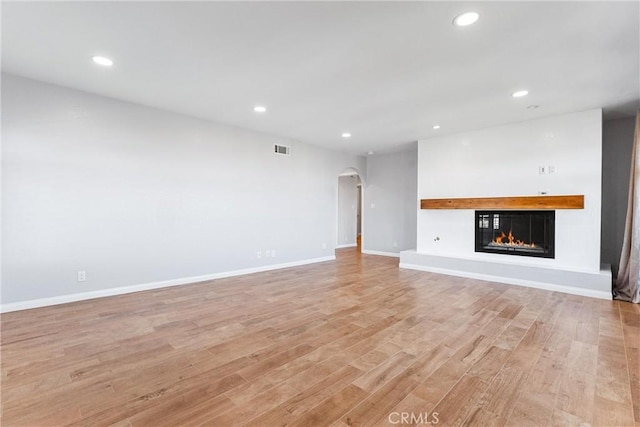 unfurnished living room with a glass covered fireplace, arched walkways, recessed lighting, and visible vents