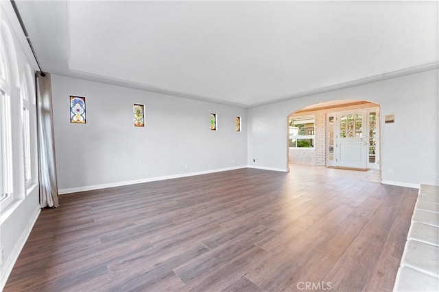 unfurnished living room featuring arched walkways, baseboards, and wood finished floors