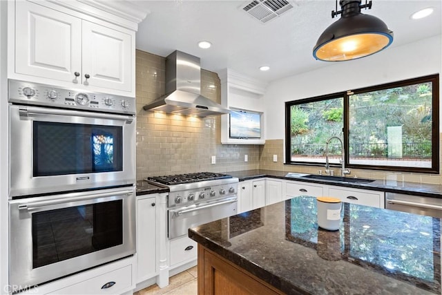 kitchen featuring visible vents, wall chimney range hood, dark stone counters, a sink, and stainless steel appliances