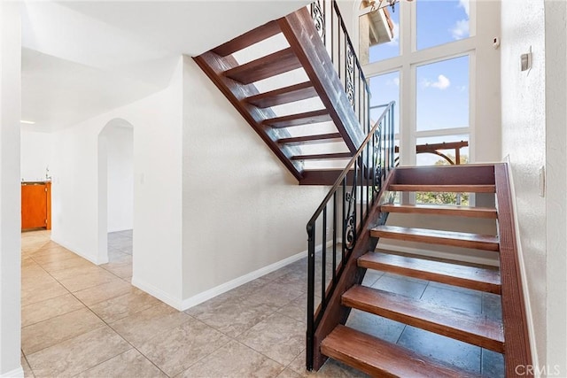 staircase featuring baseboards, arched walkways, a textured wall, and tile patterned flooring