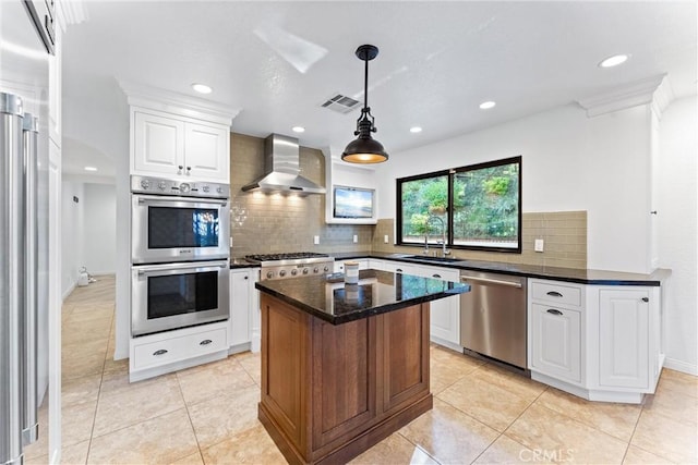 kitchen featuring visible vents, wall chimney range hood, white cabinetry, a sink, and appliances with stainless steel finishes