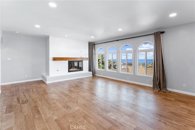 unfurnished living room featuring recessed lighting, baseboards, a glass covered fireplace, and light wood finished floors