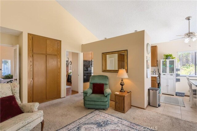 sitting room with a ceiling fan, high vaulted ceiling, light carpet, and a textured ceiling
