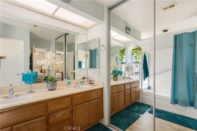 full bath with visible vents, a sink, wood finished floors, and double vanity