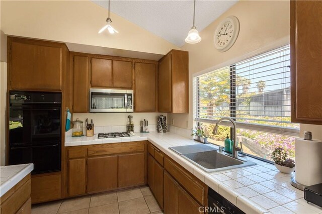kitchen featuring dobule oven black, brown cabinetry, stainless steel microwave, a sink, and vaulted ceiling