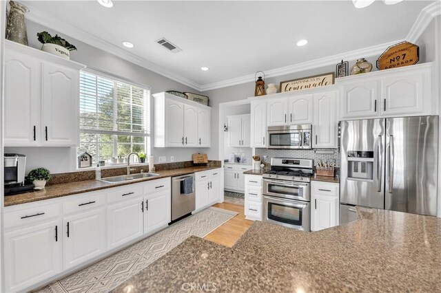 kitchen featuring visible vents, crown molding, appliances with stainless steel finishes, white cabinetry, and a sink