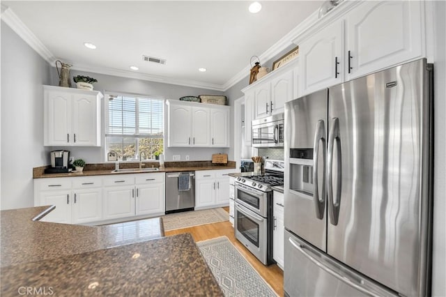 kitchen with a sink, appliances with stainless steel finishes, visible vents, dark countertops, and white cabinets