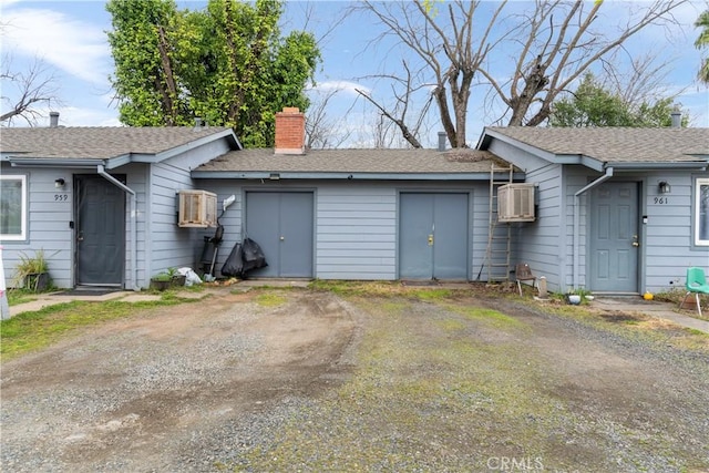 view of front facade with dirt driveway, a chimney, and a wall mounted AC