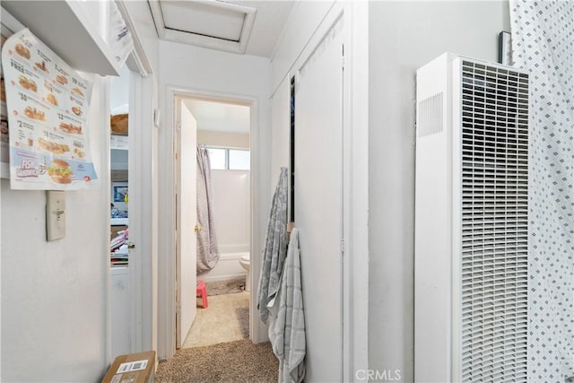 hallway featuring attic access, a heating unit, and carpet flooring