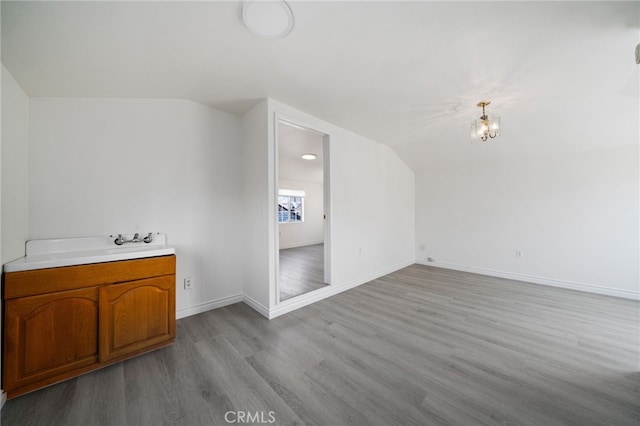 bonus room featuring vaulted ceiling, wood finished floors, baseboards, and a chandelier