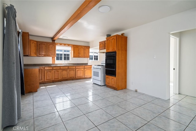 kitchen featuring beamed ceiling, white gas range oven, light tile patterned floors, brown cabinetry, and a sink