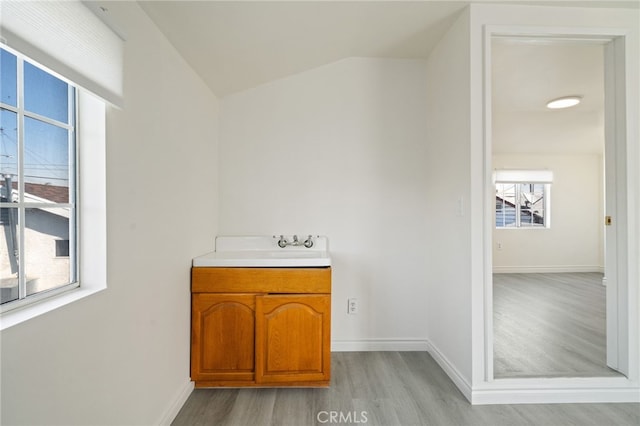 bathroom featuring lofted ceiling, wood finished floors, baseboards, and a sink