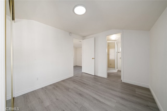 spare room featuring lofted ceiling, baseboards, and wood finished floors