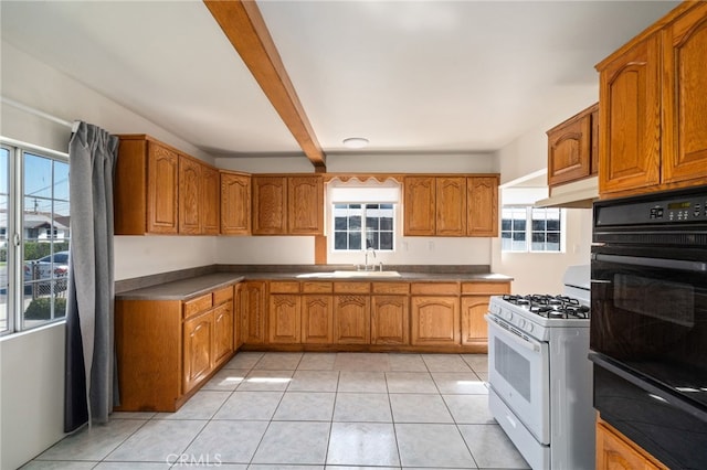 kitchen with beam ceiling, white range with gas cooktop, a sink, under cabinet range hood, and brown cabinets