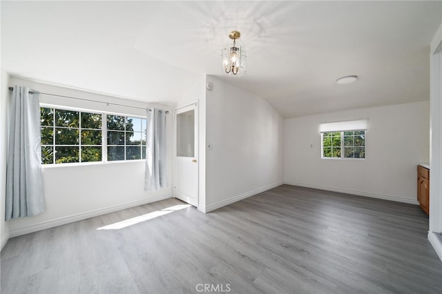 empty room with baseboards, wood finished floors, a chandelier, and vaulted ceiling