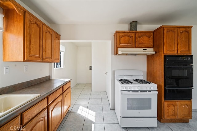 kitchen with brown cabinetry, light tile patterned flooring, white gas range oven, under cabinet range hood, and a warming drawer