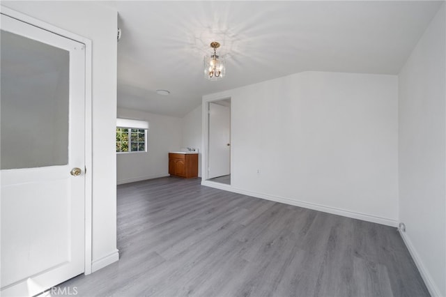 empty room featuring baseboards, an inviting chandelier, wood finished floors, and vaulted ceiling