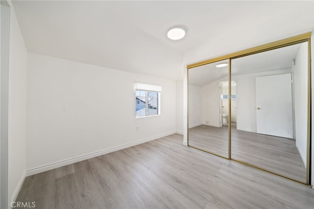 unfurnished bedroom featuring vaulted ceiling, wood finished floors, a closet, and baseboards