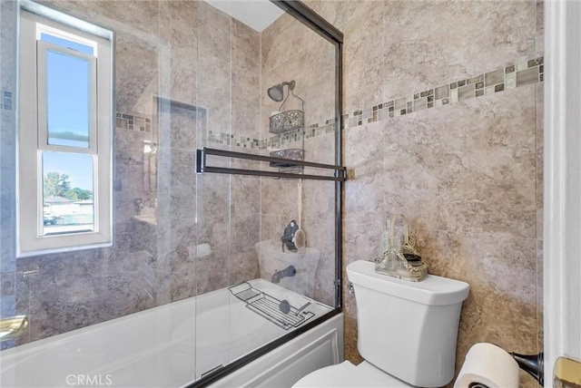 full bath featuring enclosed tub / shower combo, a healthy amount of sunlight, toilet, and tile walls