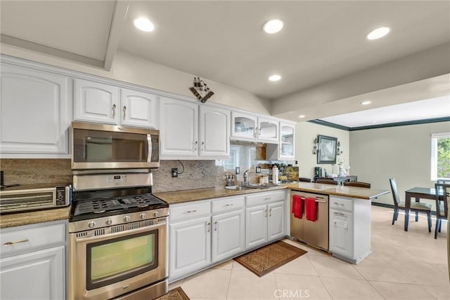 kitchen with appliances with stainless steel finishes, tasteful backsplash, a sink, white cabinets, and a peninsula