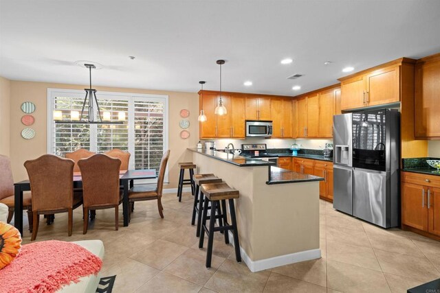 kitchen featuring a breakfast bar area, appliances with stainless steel finishes, dark countertops, a peninsula, and light tile patterned flooring