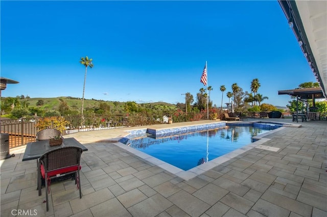 view of pool featuring a patio, fence, and a pool with connected hot tub
