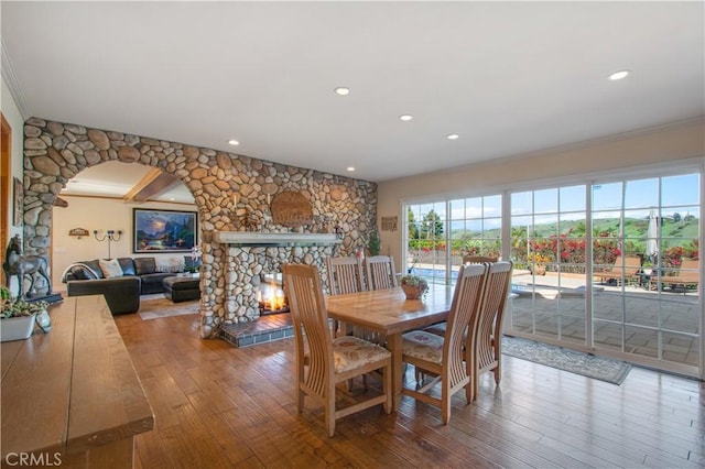 dining area with recessed lighting, hardwood / wood-style floors, ornamental molding, arched walkways, and a stone fireplace