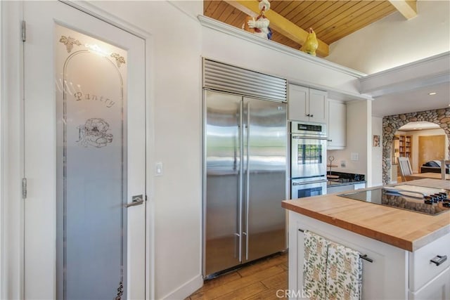 kitchen with white cabinetry, wood counters, arched walkways, light wood finished floors, and appliances with stainless steel finishes