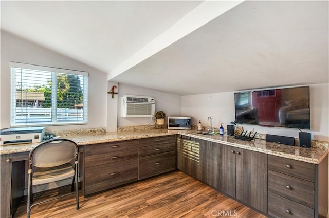 kitchen with vaulted ceiling, a wall unit AC, dark wood-style floors, stainless steel microwave, and built in desk
