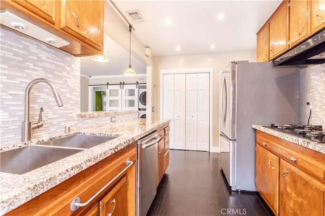 18715 Plummer St, Northridge, CA 91324 - kitchen featuring a sink, under cabinet range hood, stacked washing machine and dryer, brown cabinetry, and tasteful backsplash