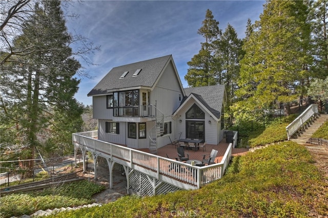 back of property featuring stairway, a balcony, a deck, and a shingled roof