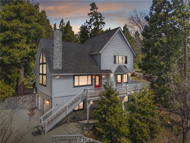view of front of property with stairway, driveway, roof with shingles, an attached garage, and a chimney