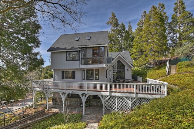 rear view of property featuring a wooden deck, a patio area, fence, and a shingled roof