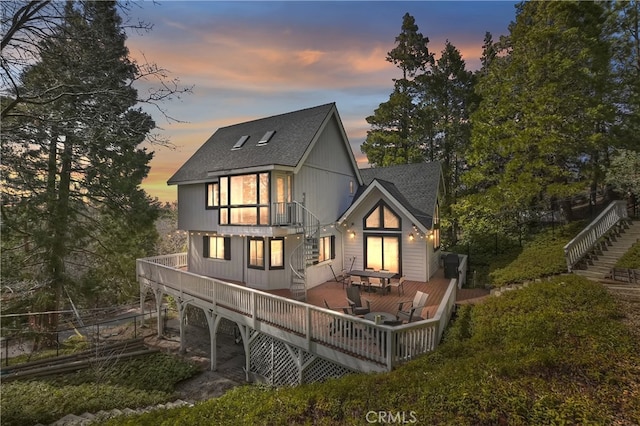 back of property at dusk with a wooden deck and roof with shingles