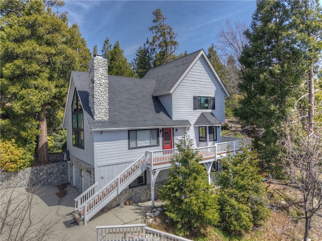 view of front of home featuring stone siding, stairway, roof with shingles, a garage, and a chimney