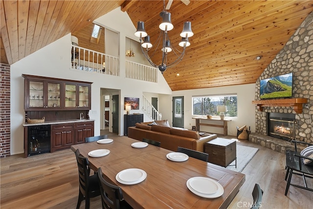 dining area featuring stairs, a stone fireplace, wine cooler, light wood-style floors, and wooden ceiling