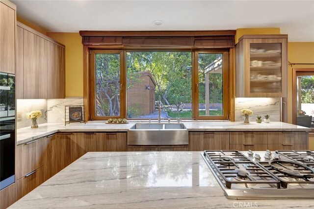 24925 Vista Verenda, Woodland Hills, CA 91367 - kitchen featuring stainless steel gas cooktop, modern cabinets, light stone countertops, tasteful backsplash, and glass insert cabinets