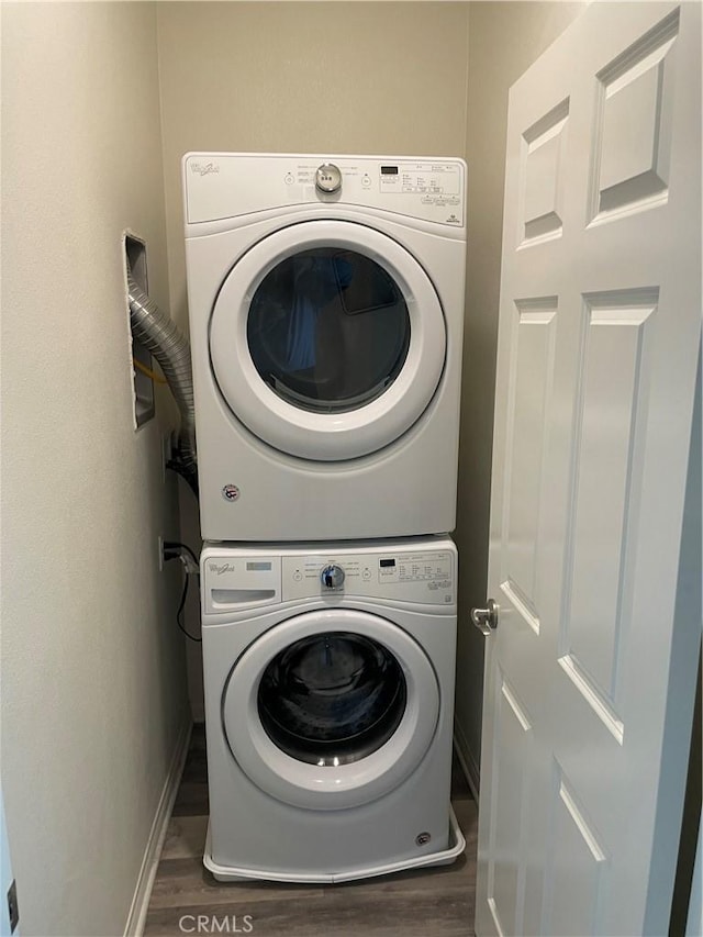 laundry area featuring baseboards, wood finished floors, stacked washer and dryer, and laundry area