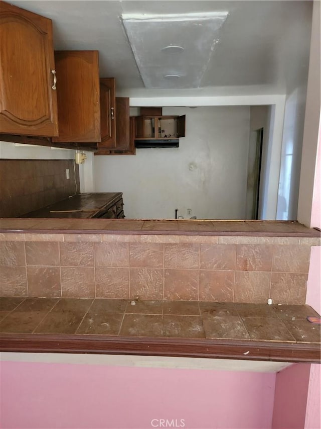 kitchen featuring backsplash, brown cabinetry, and tile countertops
