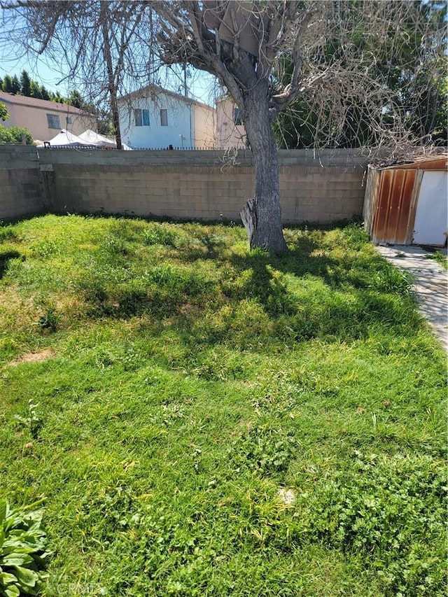 view of yard featuring a storage shed, a fenced backyard, and an outdoor structure