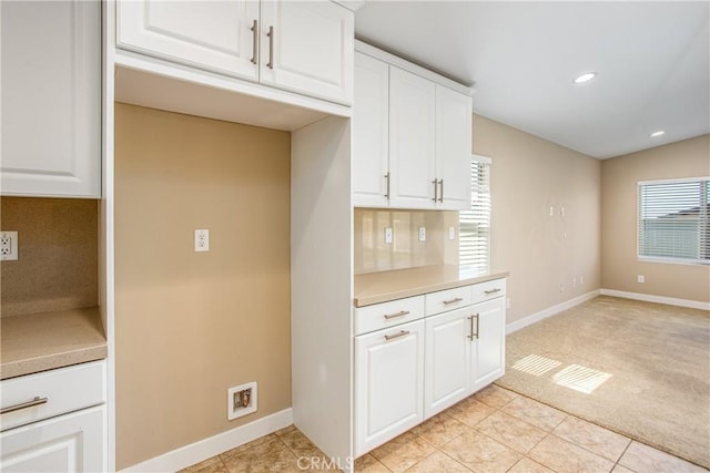 kitchen with baseboards, light countertops, backsplash, and white cabinetry